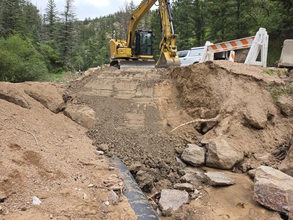 An excavator works near a buried pipe to clear some of the sediment near the washout.
