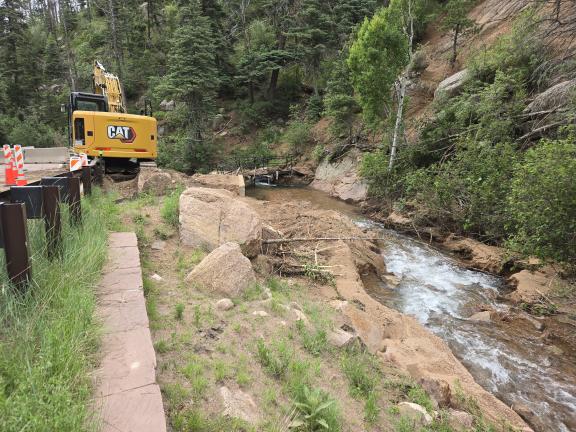 An excavator works on the bridge as water from the creek rushes by.