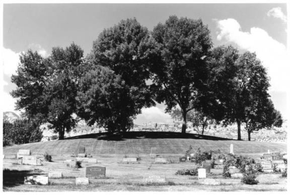 View of graves and tombstones with trees and rock formations in distance.