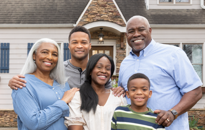 a  black family with five people in three generations smiling in front of a house.