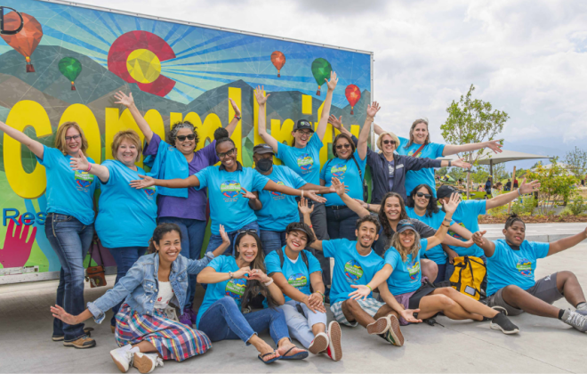 Colorado Springs residents in blue t-shirts pose for a picture in front of a truck that has artwork on it that reads "commUnity"