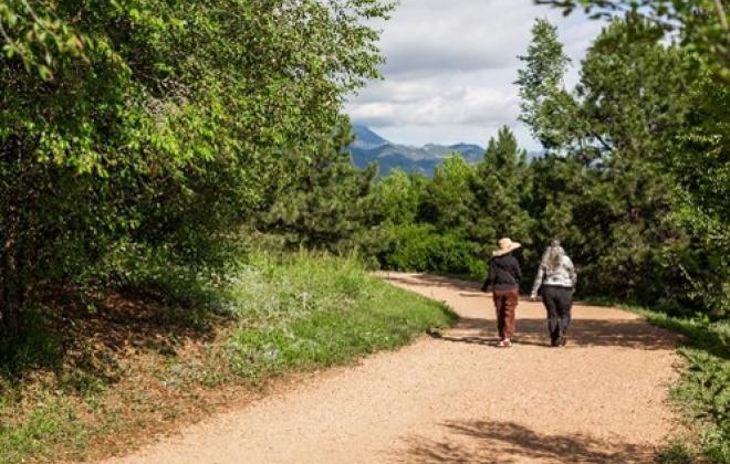 Two residents walk down a dirt path through a park on a sunny day.
